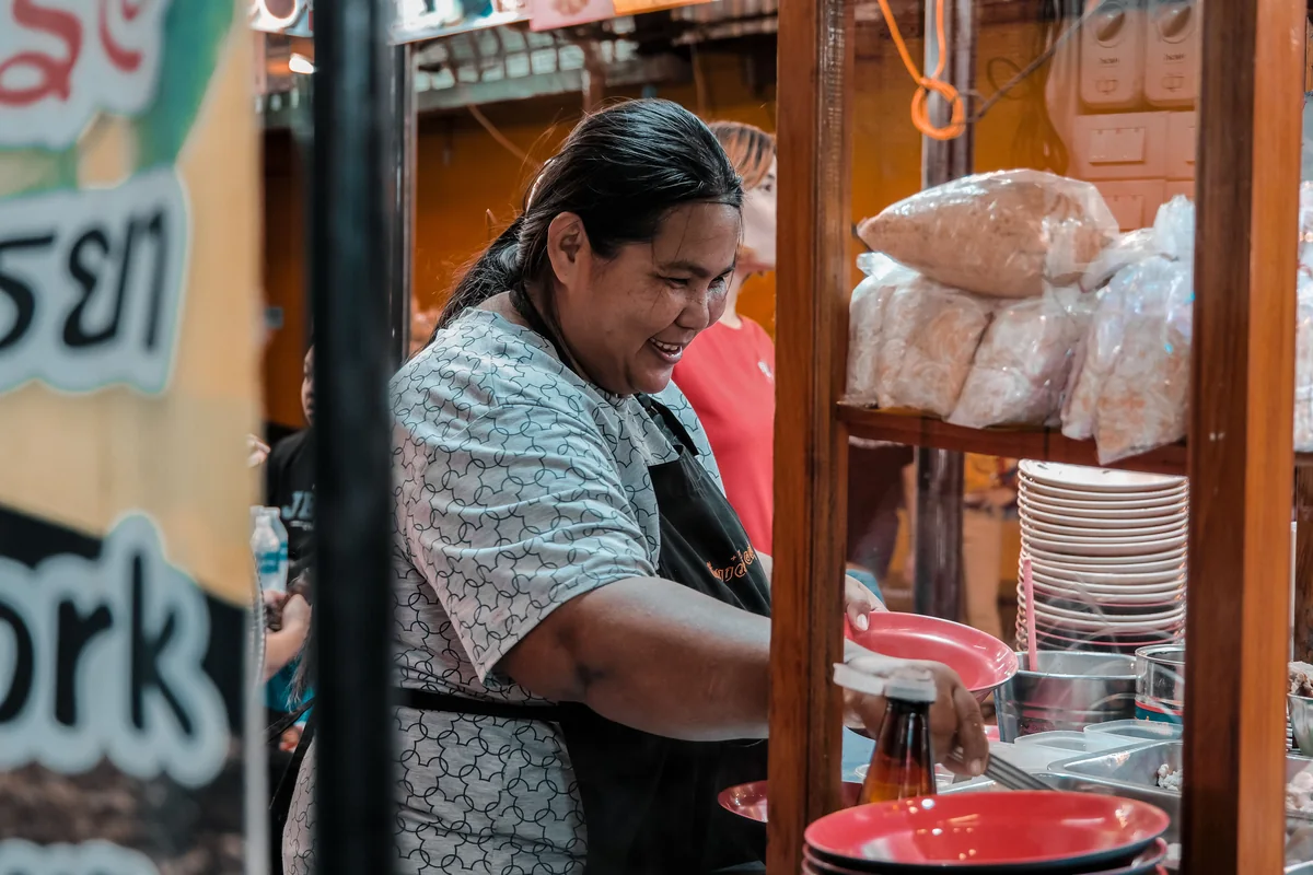 ผู้ประกอบการร้านอาหารยืนอยู่หน้าร้านของตนเองริมถนนในย่านชุมชน